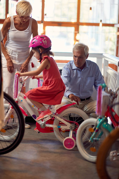grootouders kiest fiets in de fiets winkel hun kind granddaugh - Foto, afbeelding