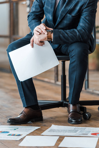 обрезанный вид бизнесмена, сидящего на стуле и держащего пустой рядом с графиками и графиками
  - Фото, изображение
