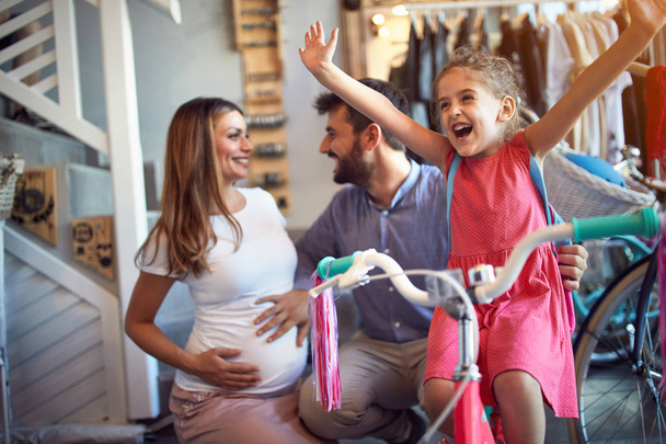 cheerful family buying new bicycle for happy girl in bike shop - 写真・画像