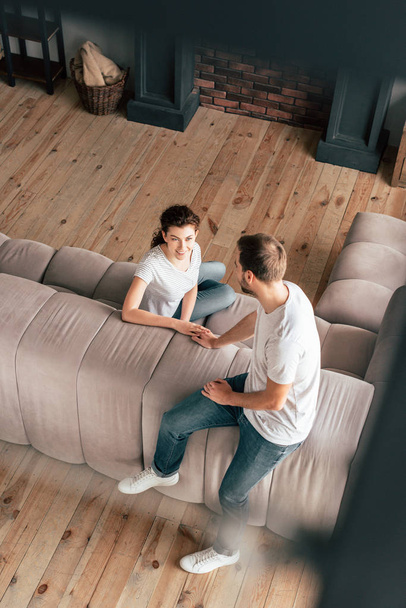 overhead view of couple sitting on sofa and touching hands in living room - Fotó, kép