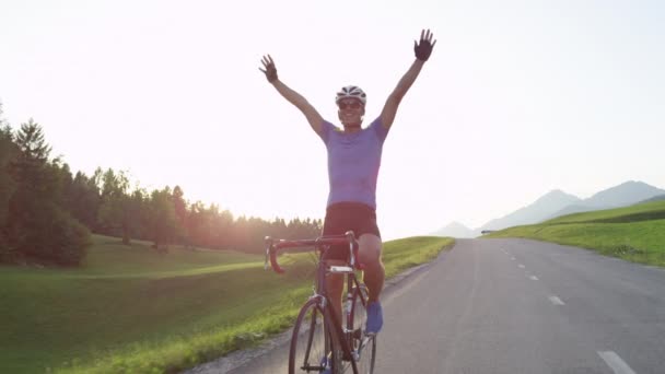 Pomalý pohyb, sluneční erupce: mladý profesionální mužský cyklista vesele jezdí po svém silničním kole bez rukou po vítězství. Atletický muž oslavuje úspěšnou cyklistickou výuku napříč malebnou krajinou. - Záběry, video