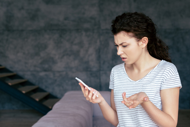 mulher irritada em t-shirt usando smartphone na sala de estar
 - Foto, Imagem