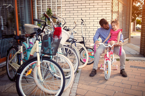 Young father shopping, new bicycle for little girl in bike shop  - Photo, Image