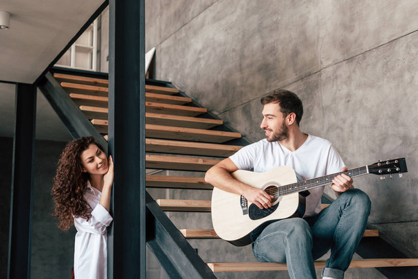 sourire barbu homme assis sur les escaliers et jouer de la guitare acoustique à petite amie
 - Photo, image