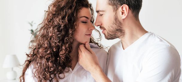 panoramic shot of handsome bearded man gently touching girlfriend at home - Фото, изображение