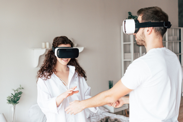 couple in vr headsets holding hands in bedroom - 写真・画像