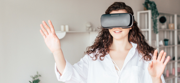 panoramic shot of smiling girl in vr headset waving hands in bedroom - Photo, Image
