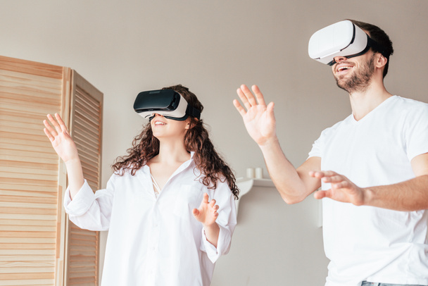 couple in vr headsets waving hands in bedroom - Photo, Image