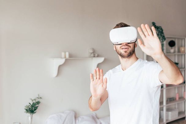 emotional man in vr headset waving hands in bedroom - Фото, изображение