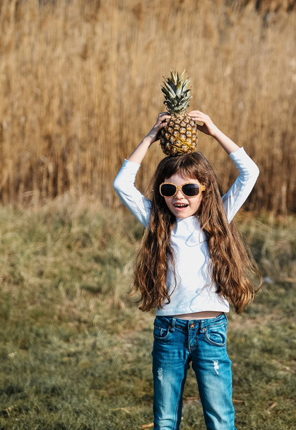 Kis aranyos lány ananász a tengerparton naplementekor. - Fotó, kép