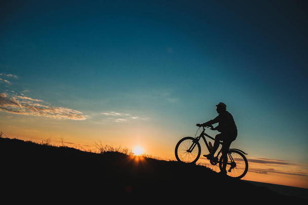 Silhouet van een mannelijke mountainbiker bij zonsondergang in de bergen - Foto, afbeelding