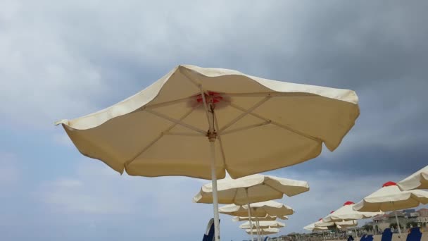 Rüzgarlı bulutlu bir günde sahilde güneşlik şemsiye - Video, Çekim