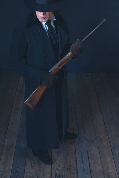 Βικτοριανό άνθρωπος με μακρύ μαύρο παλτό και καπέλο κρατώντας τουφέκι. - Φωτογραφία, εικόνα