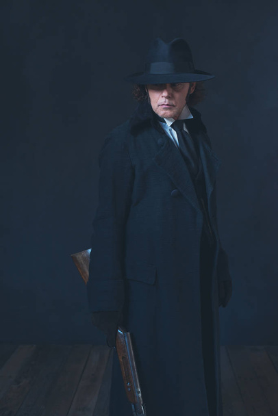 Victoriaanse man in lange zwarte jas en hoed Holding Rifle. - Foto, afbeelding