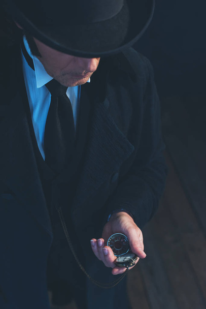 Homme édouardien en long manteau noir et chapeau tenant montre de poche
. - Photo, image