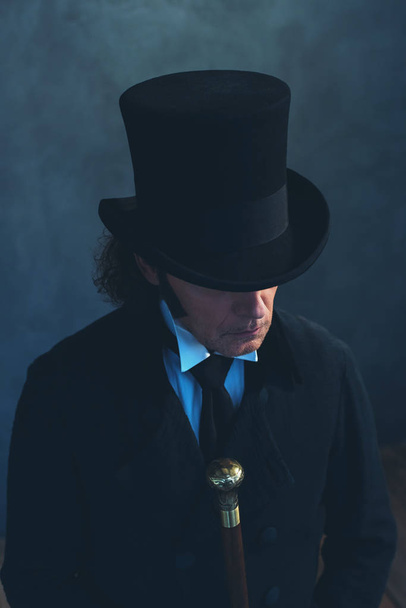 Edwardian man in long black coat and hat holding cane. - Foto, Bild