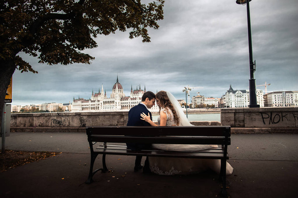 Nevěsta a ženich seděli na lavici u řeky ve starém městě. Močení v Budapešti - Fotografie, Obrázek