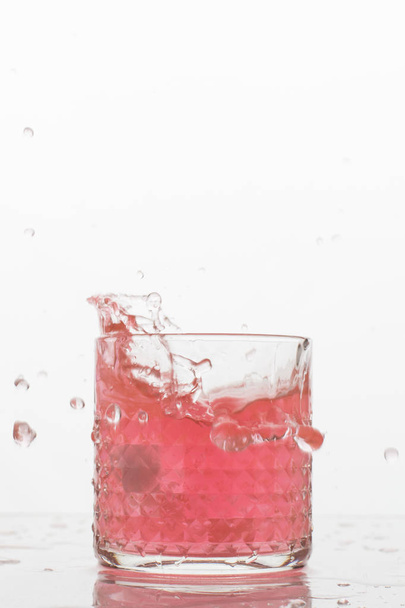 A glass of fresh drink with splashes on white background. Frozen motion. Trendy color 2019, coral - Foto, imagen