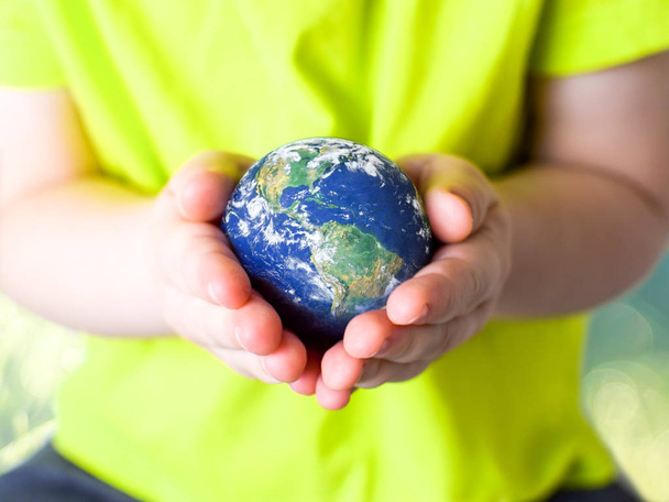 Small child in a green T-shirt gently holding the planet Earth in her hands. Earth day. Green concept - Photo, image