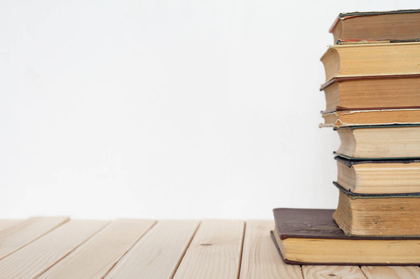 Una pila de libros antiguos para negocios y educación sobre una superficie de madera contra una pared blanca
. - Foto, Imagen