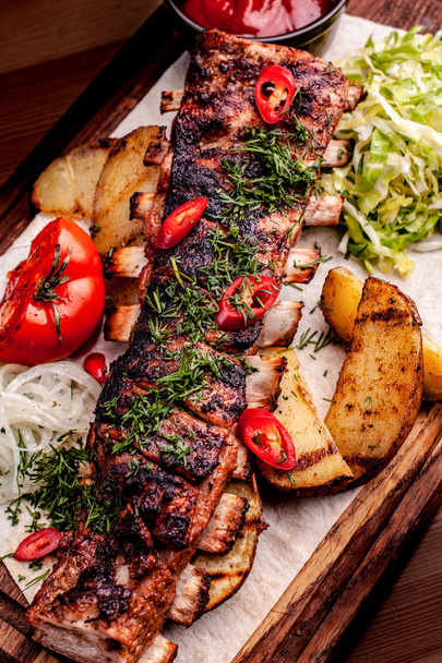 Delicious barbecued ribs seasoned with fresh herbs, cabbage salad, backed potato on an old rustic wooden chopping board - Foto, Bild