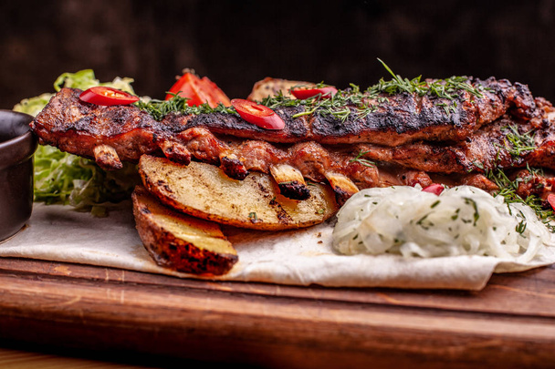 Delicious barbecued ribs seasoned with fresh herbs, cabbage salad, backed potato on an old rustic wooden chopping board - Fotografie, Obrázek