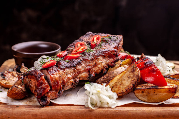 Delicious barbecued ribs seasoned with fresh herbs, cabbage salad, backed potato on an old rustic wooden chopping board - Photo, image