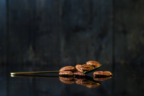 Pecan in a spoon on a mirror, black background, side view. - Foto, afbeelding