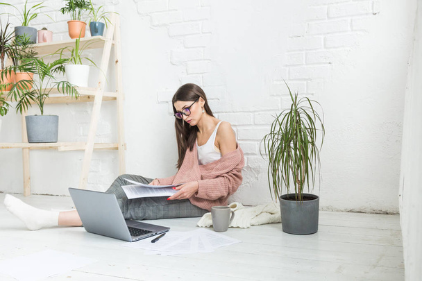 Young woman sits on the floor in a Scandinavian apartment interior with a laptop, studying law, freelance girl at work, distance learning student, online employment, paperwork and outsourcing concept - Foto, afbeelding