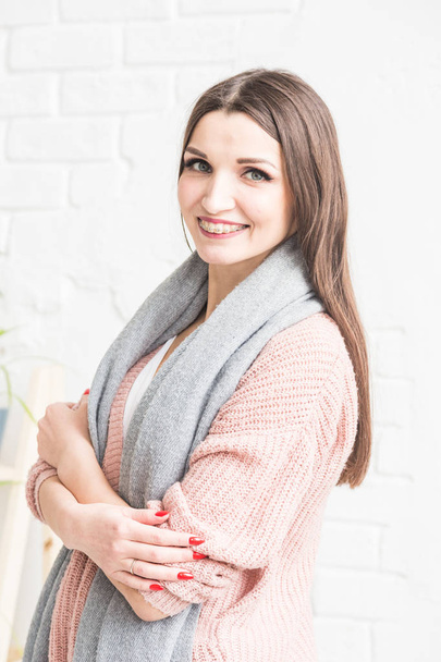 Portrait of a beautiful young brunette woman in a sweater with a scarf on a light background. - Foto, Bild