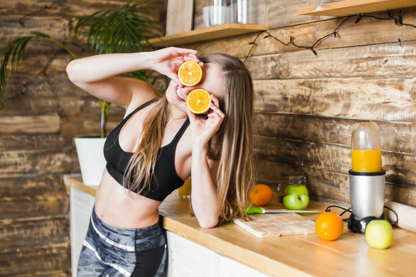 Attractive girl in sportswear is having fun, putting halves of orange to her eyes. The benefits of healthy eating, fitness and beauty - Foto, afbeelding