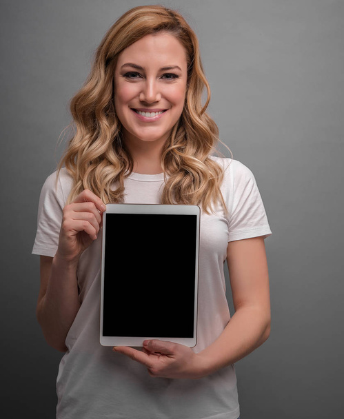 attraktive Blondine hält Tablet-PC auf grauem Hintergrund. - Foto, Bild