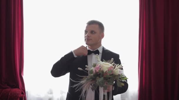 結婚式の花の束と窓の近くに立っているハンサムな新郎 - 映像、動画