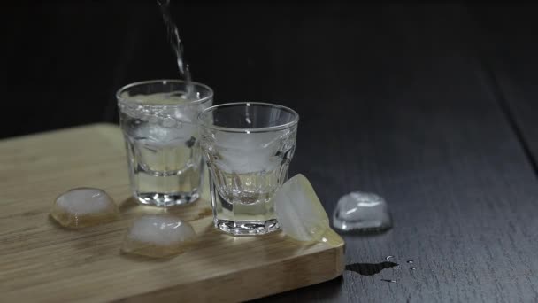 Ρίξτε βότκα από ένα μπουκάλι σε γυαλιά shot με παγάκια - Πλάνα, βίντεο