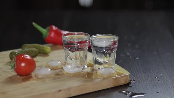 Vodka in shot glasses on rustic wood board. Adding ice cubes. - Video, Çekim
