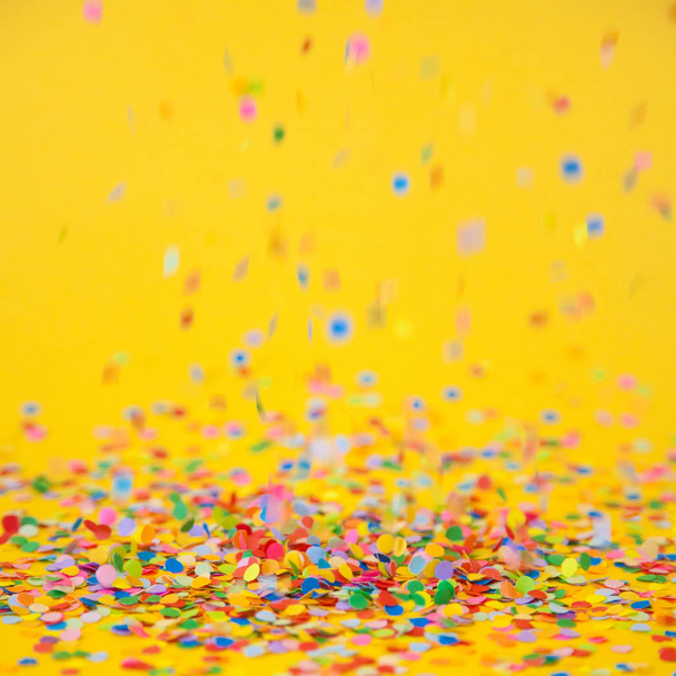 Colored confetti flying on yellow background - Φωτογραφία, εικόνα