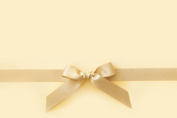 Gold ribbon with a bow as a gift on a beige background - Foto, Imagen