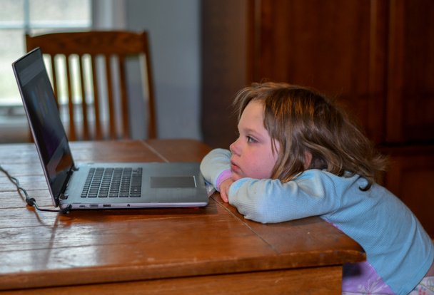 niño en pijama se relaja en la mesa con la computadora portátil de la abuela, viendo videos de canciones de los niños
 - Foto, imagen