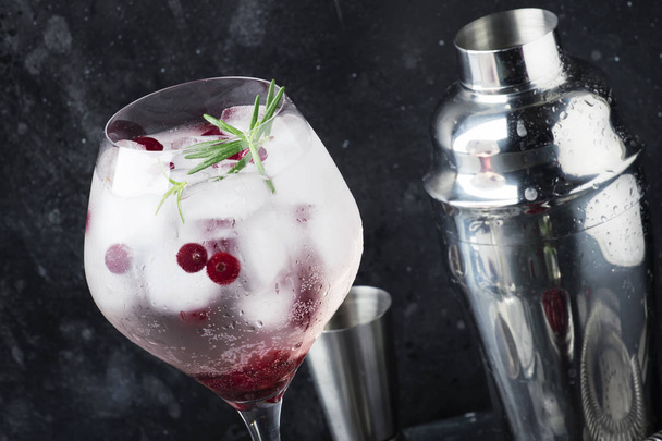 Cranberry cocktail with ice, fresh rosemary and red berries in big wine glass, bar tools, gray bar counter background, copy space, selective focus - Фото, изображение