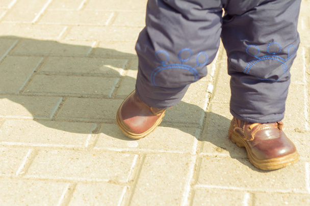 ένα μικρό παιδί σε μπότες περπατάει στο δρόμο την άνοιξη σε μια ηλιόλουστη μέρα - Φωτογραφία, εικόνα