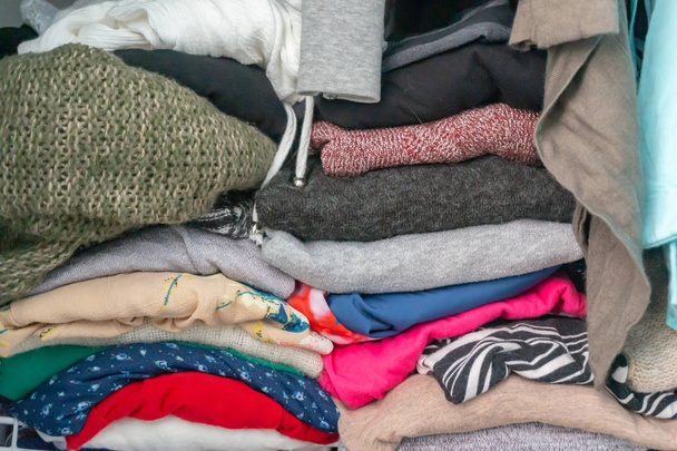 zusammengepferchte gefaltete Pullover und Kleidungsstücke aus dem Kleiderschrank einer Frau in einem Schrank. Exzesse, die Notwendigkeit, Kleiderschränke zu organisieren, aufzuräumen, zu reinigen oder Kleidung zu spenden. - Foto, Bild
