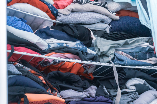 Niebieskie i czerwone odcienie odzieży w kobiecej szafie, składany, ale brudny, w potrzebie organizacji szafie. Przedstawianie podarowania ubrań, sprzątania, konsumpcjonizmu itp.. - Zdjęcie, obraz