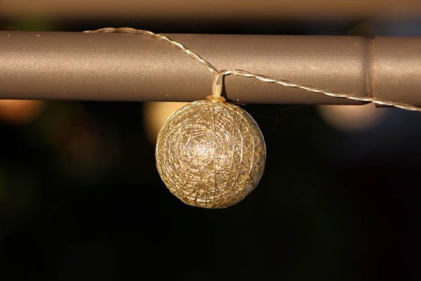 Zlatý drát vánoční ozdoba s vnitřním LED světlem visel z kovového pólu elektrickými dráty čekajícího na zahradní večírek za teplého slunečného dne - Fotografie, Obrázek