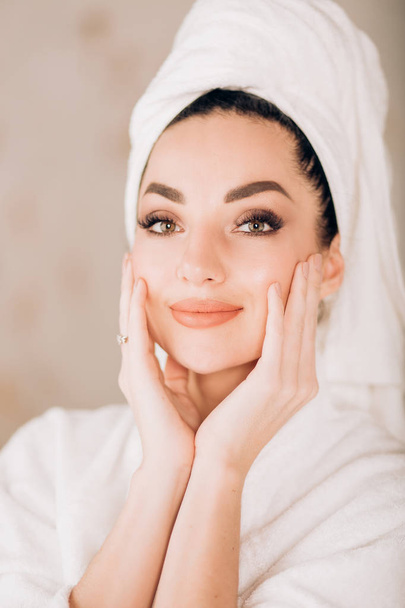 Attractive girl wearing white bathrobe and towel on head in bathroom - Photo, Image