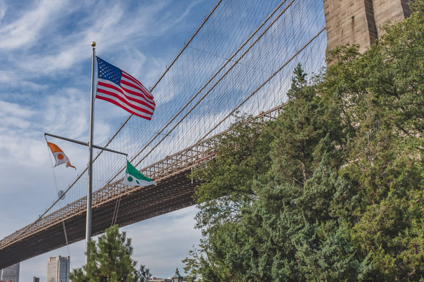 US flag flying against Brooklyn Bridge, in Brooklyn Bridge Park, New York, USA - Zdjęcie, obraz