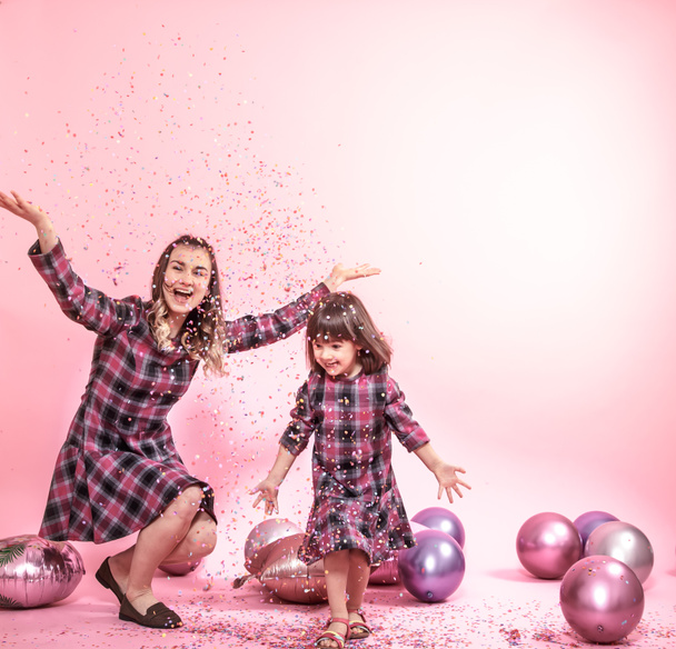 Zabawny Mama i dziecko na różowym tle. Mała dziewczynka i matka, zabawy z balonami i konfetti - Zdjęcie, obraz