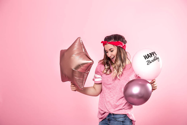 風船でピンクの t シャツで面白い女の子お誕生日おめでとうピンクの背景の笑顔や感情を与える - 写真・画像