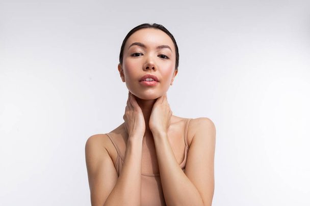 Skinny model with natural makeup touching her neck while posing - 写真・画像