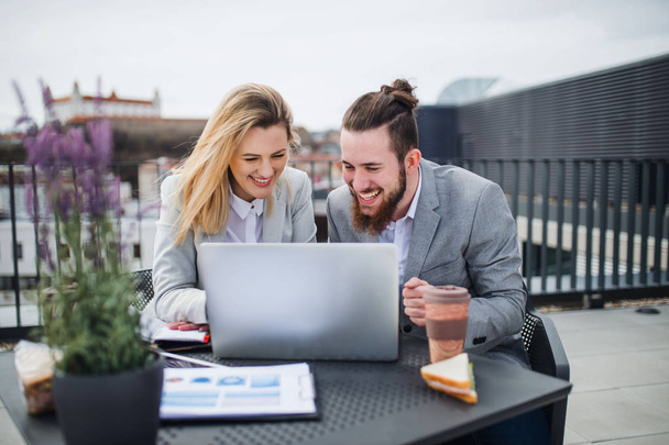Two young business people with laptop sitting on a terrace outside office, working. - Foto, imagen