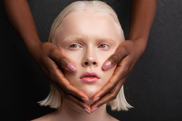 Dark-skinned hands with light pink nails touching white face - 写真・画像
